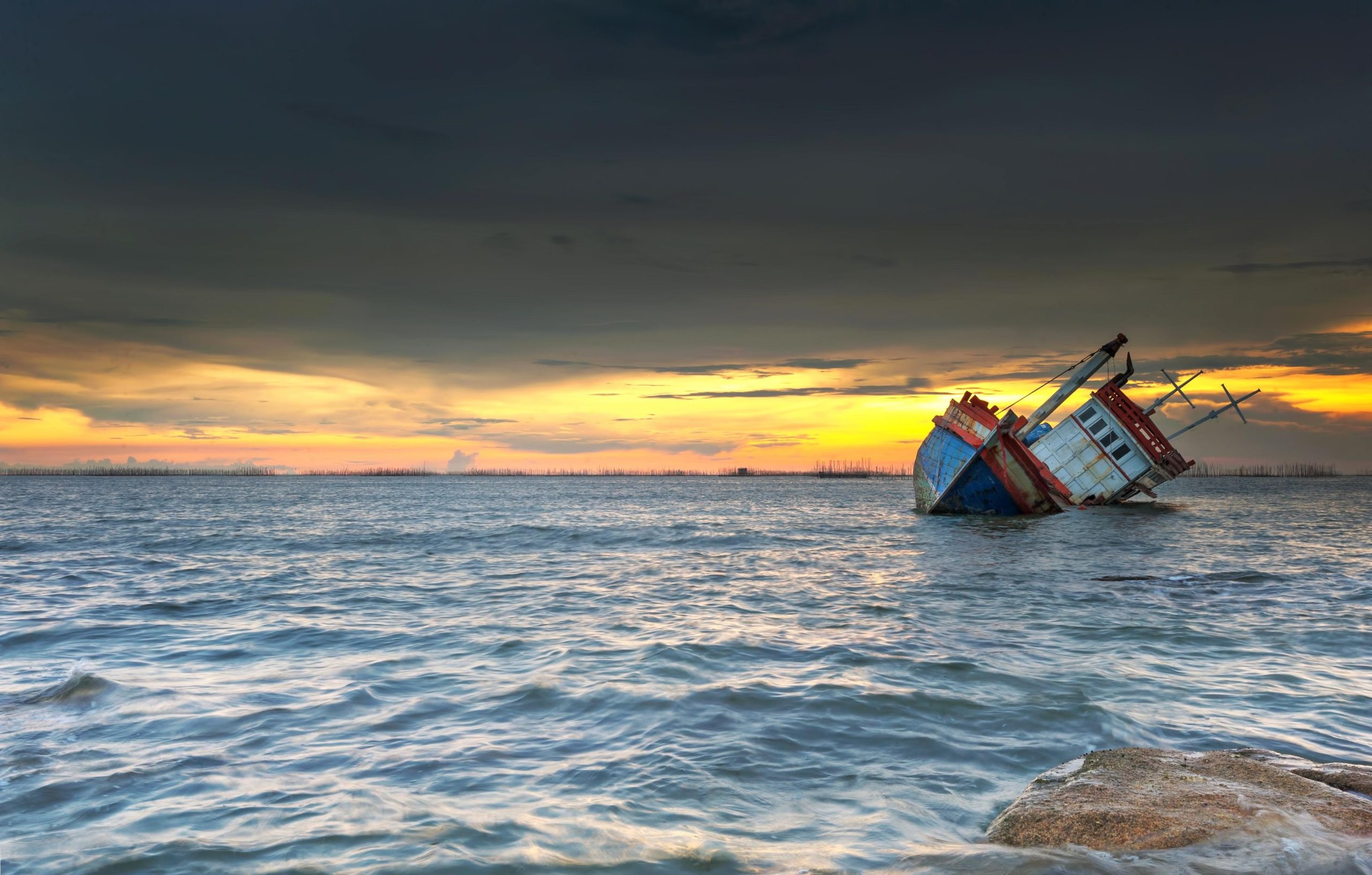 A view of the ocean with a boat that is capsized
